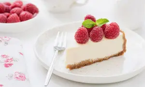 Una fetta di torta fredda allo yogurt, guarnita con lamponi freschi e menta, su un piatto con forchetta.