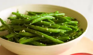 Fagiolini freschi saltati in padella con aglio e pepe, serviti in una ciotola di legno.