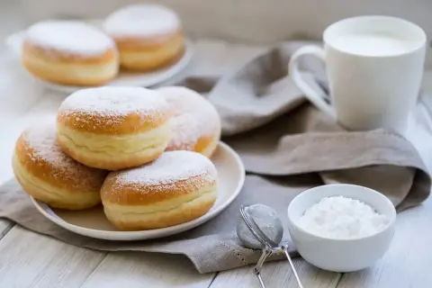 Un mucchio di soffici bomboloni alla crema, spolverati di zucchero a velo, pronti per essere gustati con una tazza di latte.