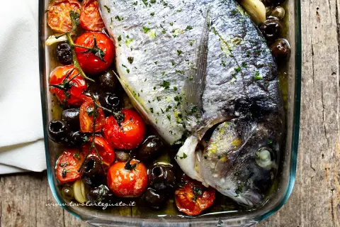 Orata al forno con pomodorini, olive nere e aglio, un piatto semplice e gustoso pronto per essere infornato.