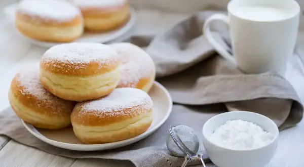 Un mucchio di soffici bomboloni alla crema, spolverati di zucchero a velo, pronti per essere gustati con una tazza di latte.