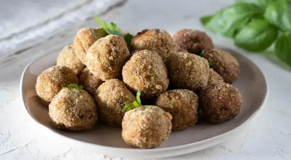 Un piatto colmo di polpette di melanzane, dorate e croccanti, pronte per essere gustate. La ricetta originale che conquista tutti.