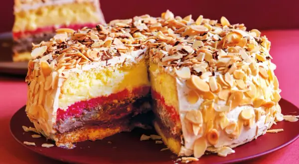 Una fetta di pizza dolce abruzzese, con strati di crema, cioccolato e confettura, ricoperta di mandorle tostate e panna.