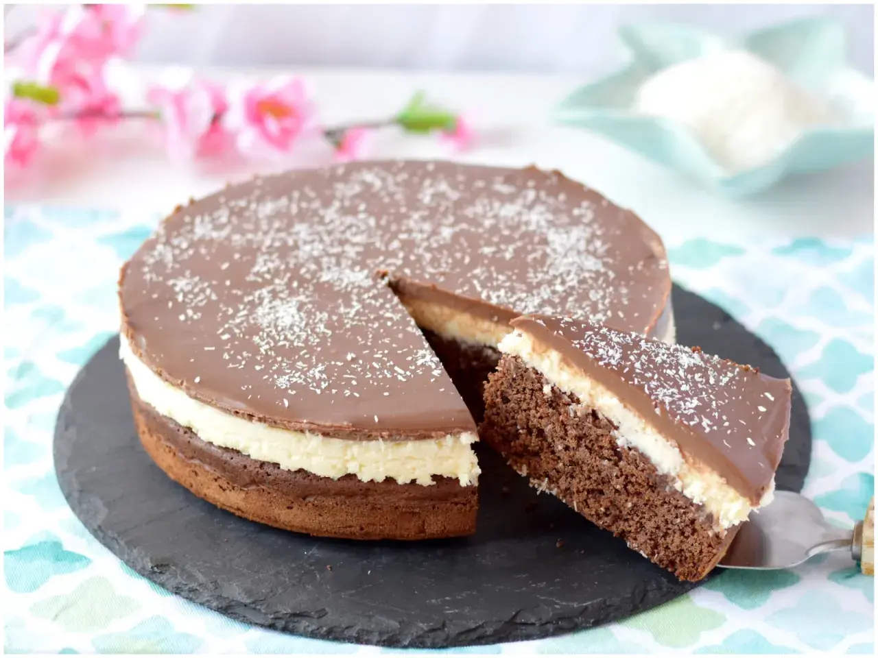 Deliziosa torta cocco e cioccolato con glassa lucida e cocco grattugiato. Una fetta è già servita.