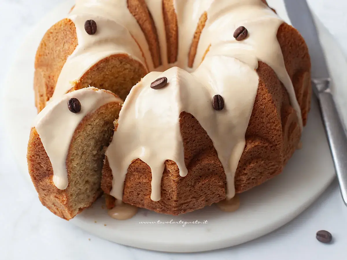 Una deliziosa torta al caffè, con glassa chiara e chicchi di caffè come decorazione. Una fetta è stata tagliata, rivelando l'interno soffice.