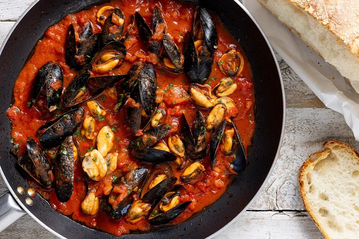 Cozze alla tarantina fumanti in padella, con pomodoro e pane fresco a lato, pronte per essere gustate.