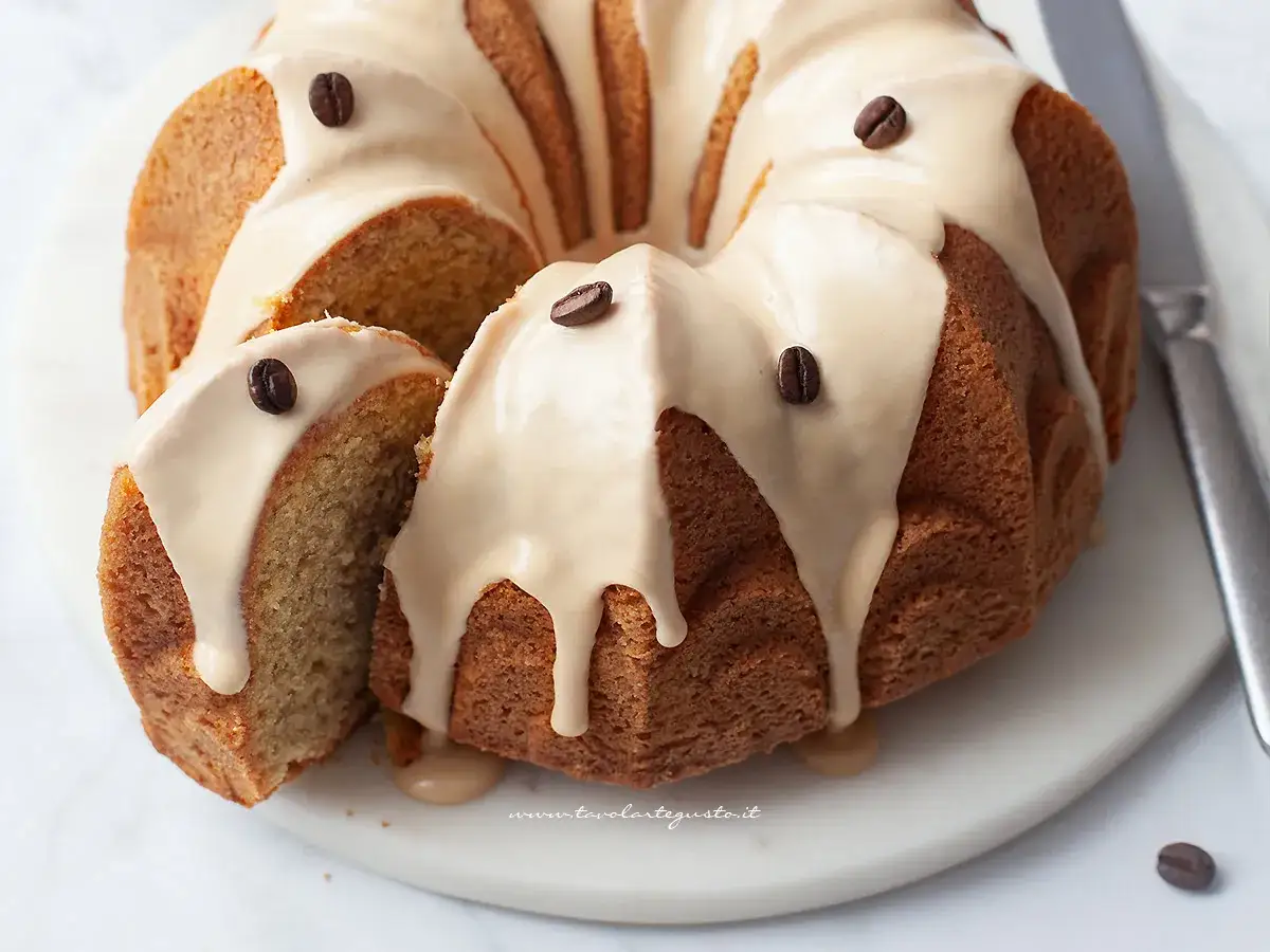 Deliziosa torta al caffè con glassa chiara e chicchi di caffè come decorazione. Una fetta è stata tagliata, mostrando la morbidezza dell'impasto.
