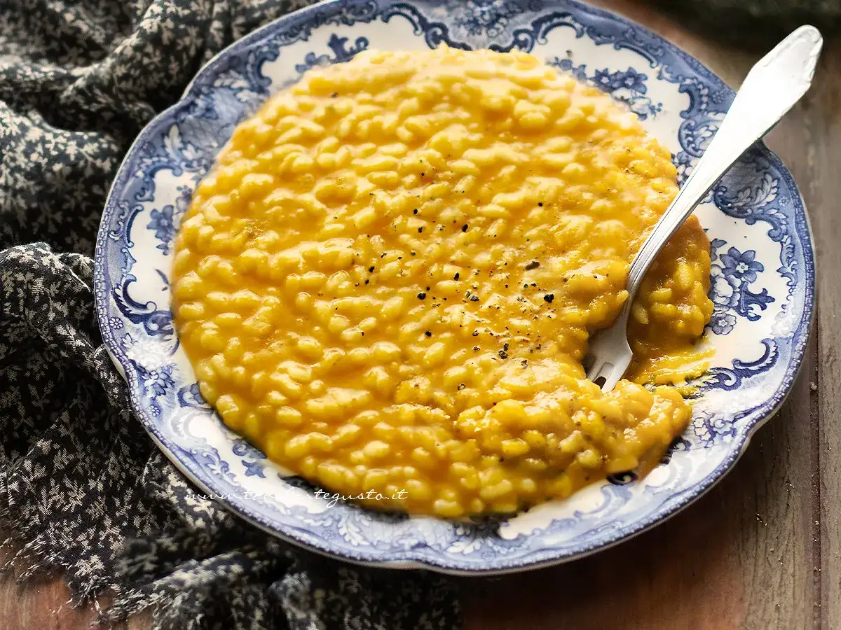 Un cremoso risotto alla zucca, cosparso di pepe nero, servito su un piatto decorato con un motivo blu e bianco.