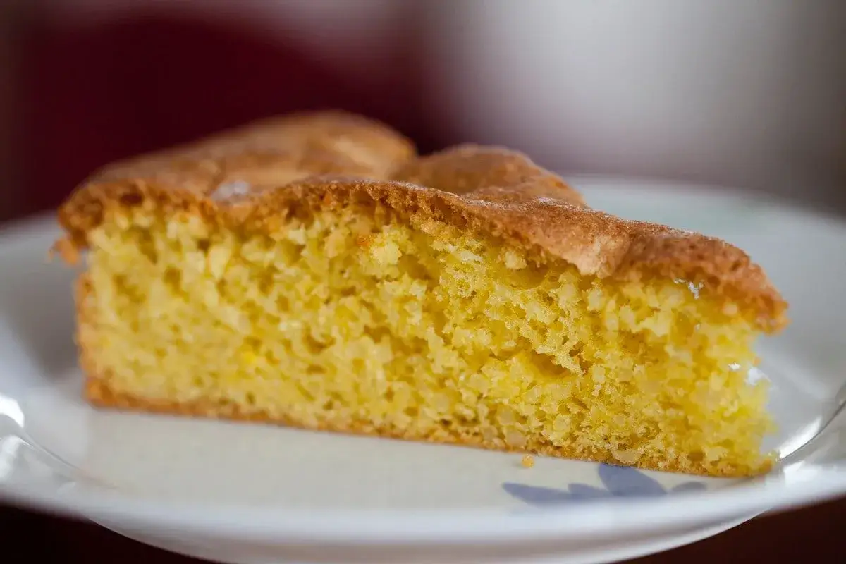 Una fetta di torta soffice e dorata, preparata con farina di mandorle, servita su un piatto bianco.