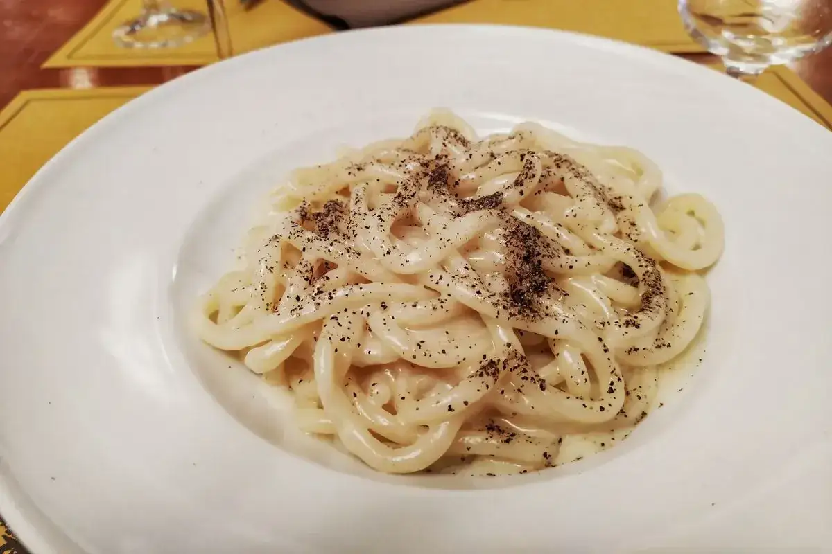 Piatto di pici cacio e pepe, pasta fresca condita con una cremosa salsa al formaggio e pepe nero macinato.