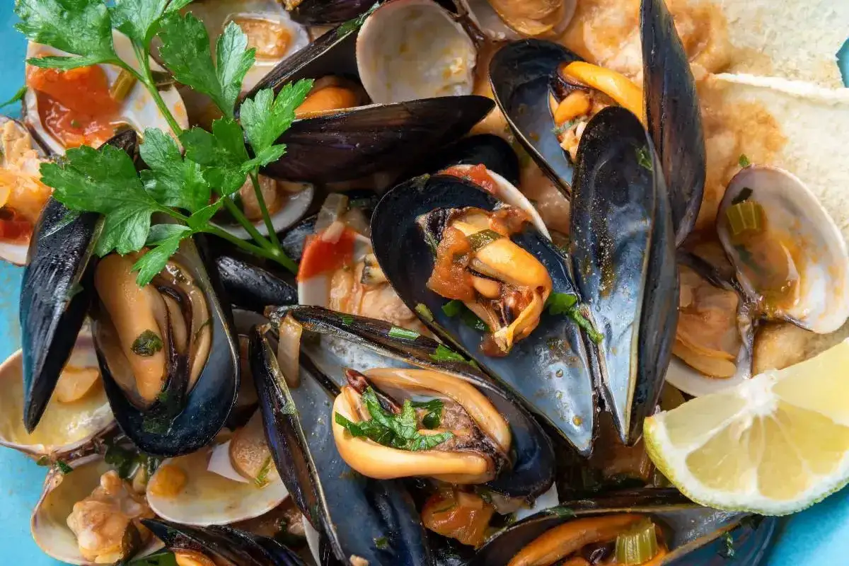 Un invitante sautè di cozze e vongole, profumato di prezzemolo e servito con fette di pane tostato e spicchi di limone.