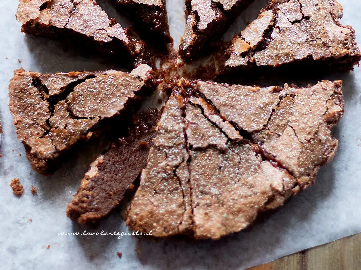 Fetta di torta con cioccolato avanzato, cosparsa di zucchero a velo, con una crosta crepata e un interno umido.