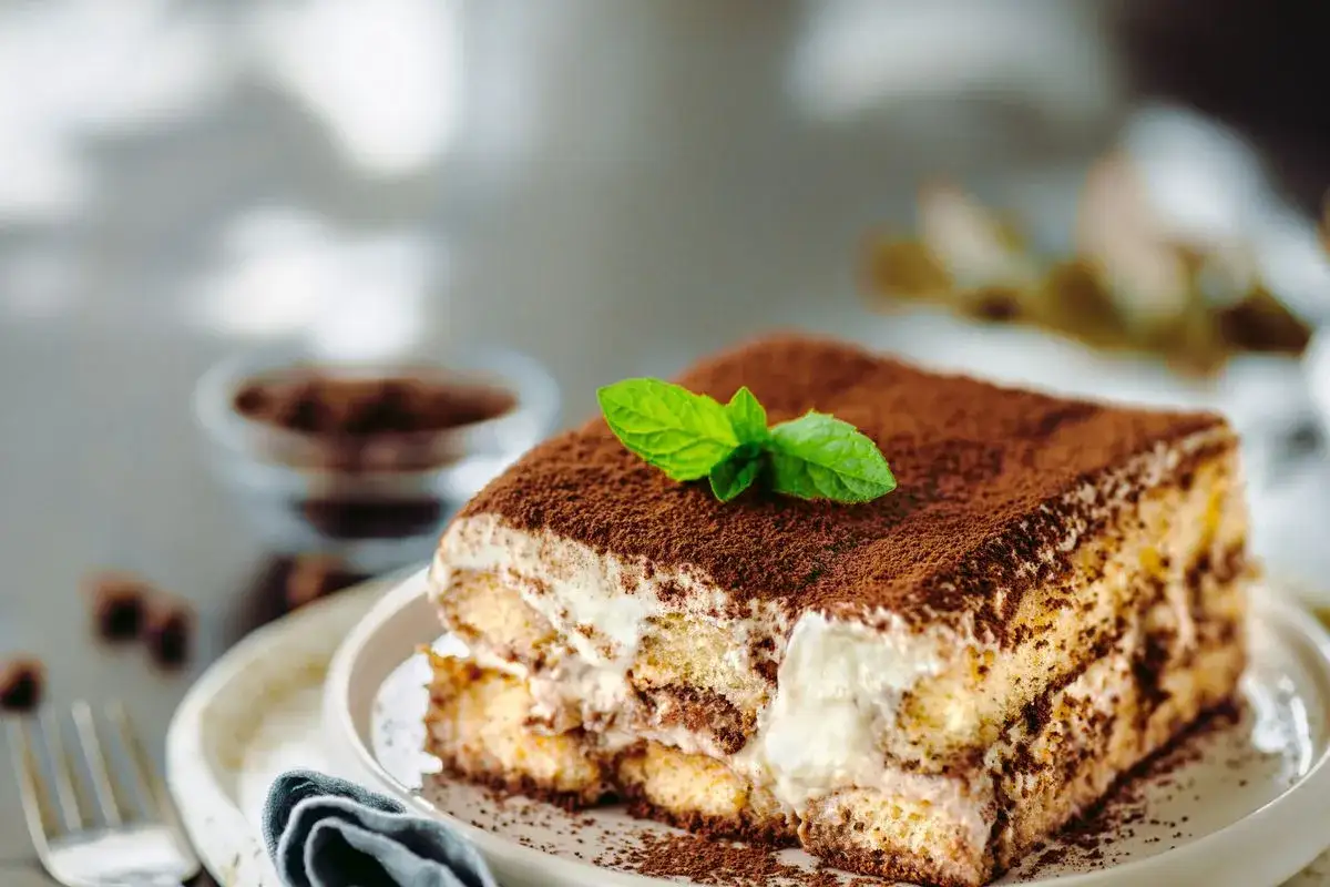 Una fetta di ricetta tiramisù classico, con savoiardi, crema e cacao, guarnita da una fogliolina di menta.