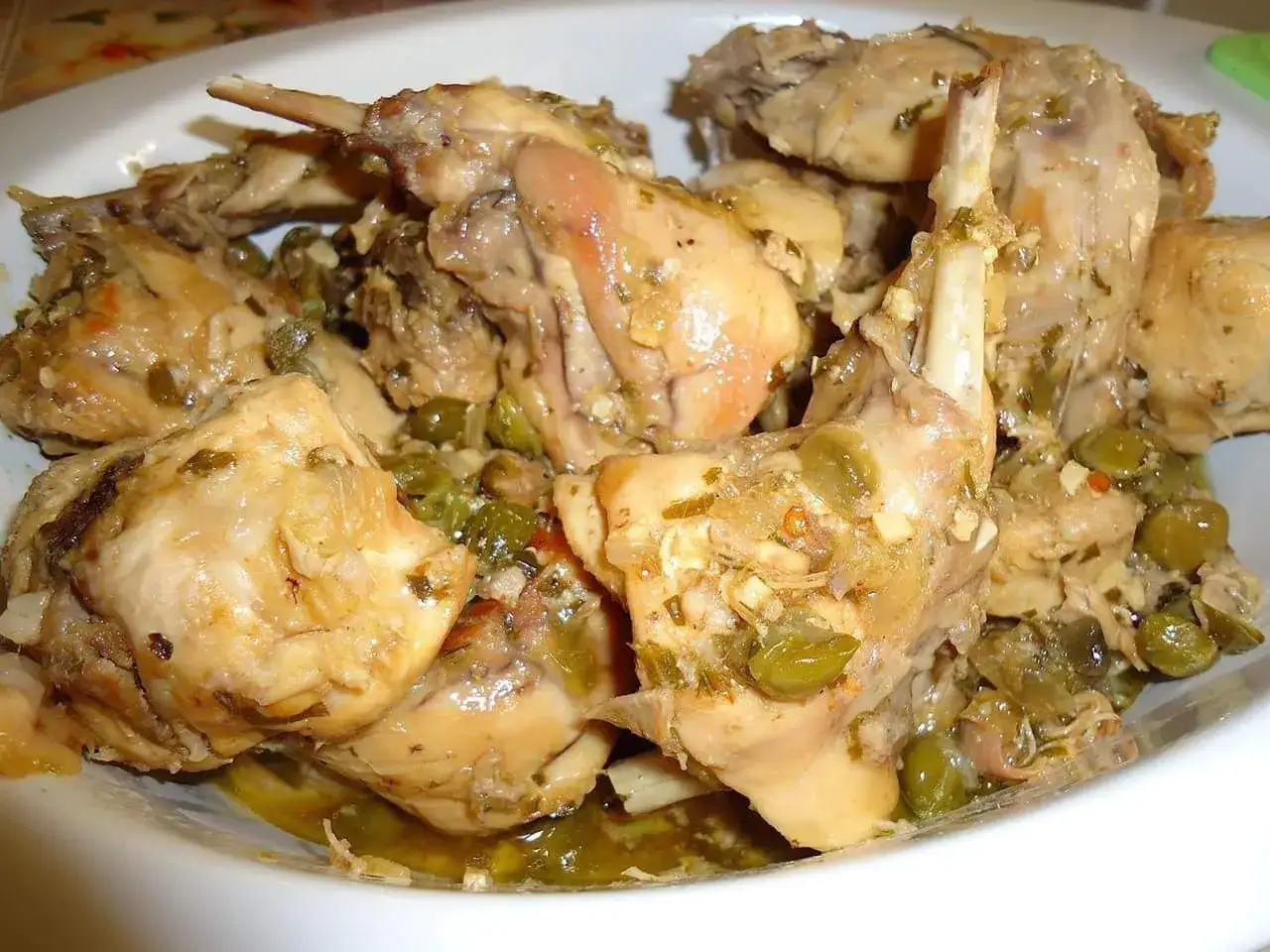 Un invitante piatto di coniglio alla cacciatora in bianco, con olive verdi e erbe aromatiche.