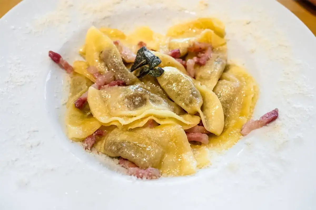 Casoncelli alla bergamasca, pasta ripiena con pancetta e salvia, cosparsi di formaggio grattugiato su un piatto bianco.