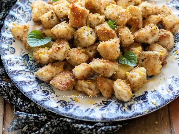 Bocconcini di pollo dorati e croccanti, guarniti con scorza di limone e foglie di menta fresca su un piatto decorato.