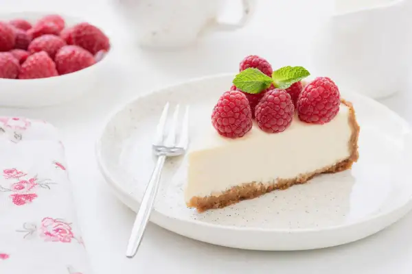 Una fetta di torta fredda allo yogurt, guarnita con lamponi freschi e menta, su un piatto con forchetta.