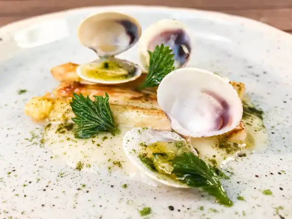 Delizioso piatto con pesce bianco, gamberi e **lupini di mare** in una salsa cremosa, guarnito con erbe fresche.